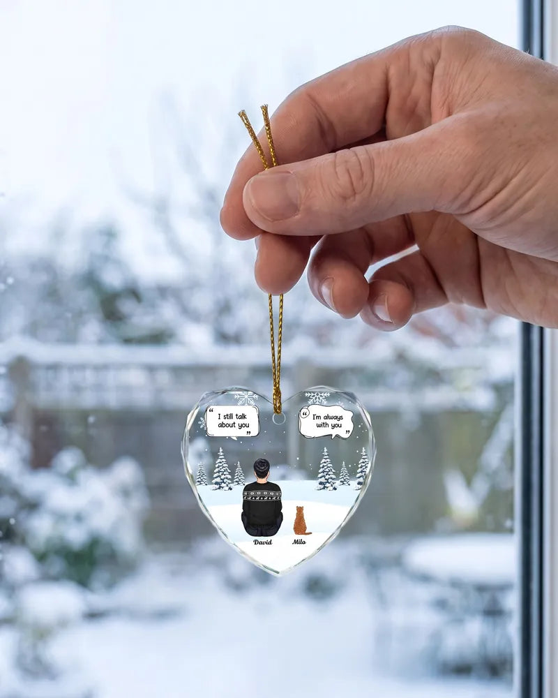 Hand holding a personalized glass heart pet memorial ornament by a snowy window