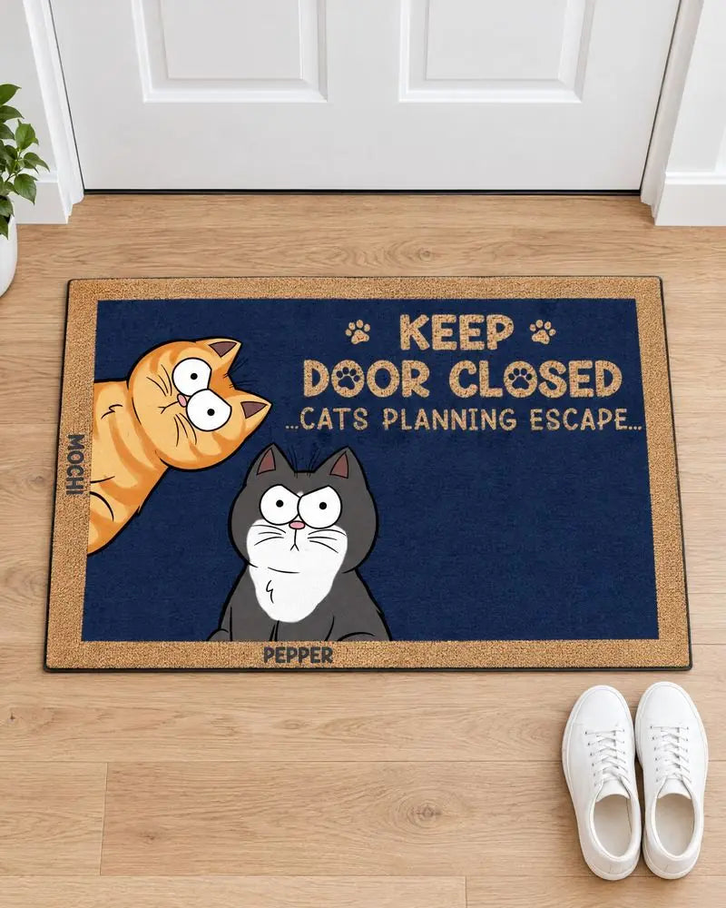 A navy KEEP DOOR CLOSED doormat with two cats, MOCHI and PEPPER, in a white entryway